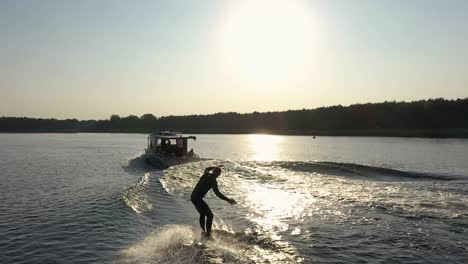 Surfer-on-surfboard-surfing-waves-behind-boat-in-sunset-003