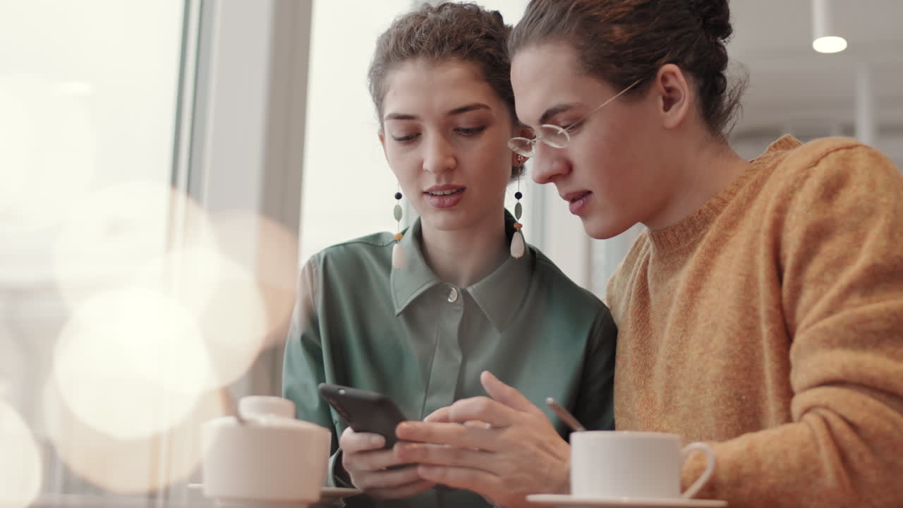 dos jóvenes usando el teléfono en un café