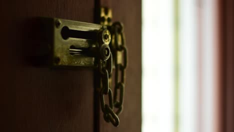 Beautifully-shot-close-up-of-an-unlocked-bolt-and-chain-on-the-inside-of-a-residential-door,-with-a-hand-sliding-the-bolt-into-place-and-engaging-the-chain,-with-stylish-bokeh