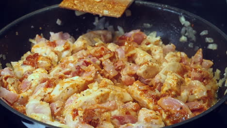 chicken curry simmers, bubbles in pan, stirred with wooden spatula