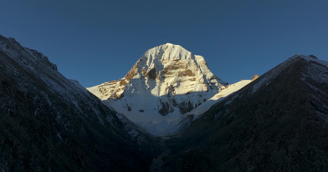 Ripresa aerea della sacra vetta del Monte Kailash, Tibet, Cina, illuminata dalla luce dorata dell'alba lungo il circuito della kora sotto il cielo blu