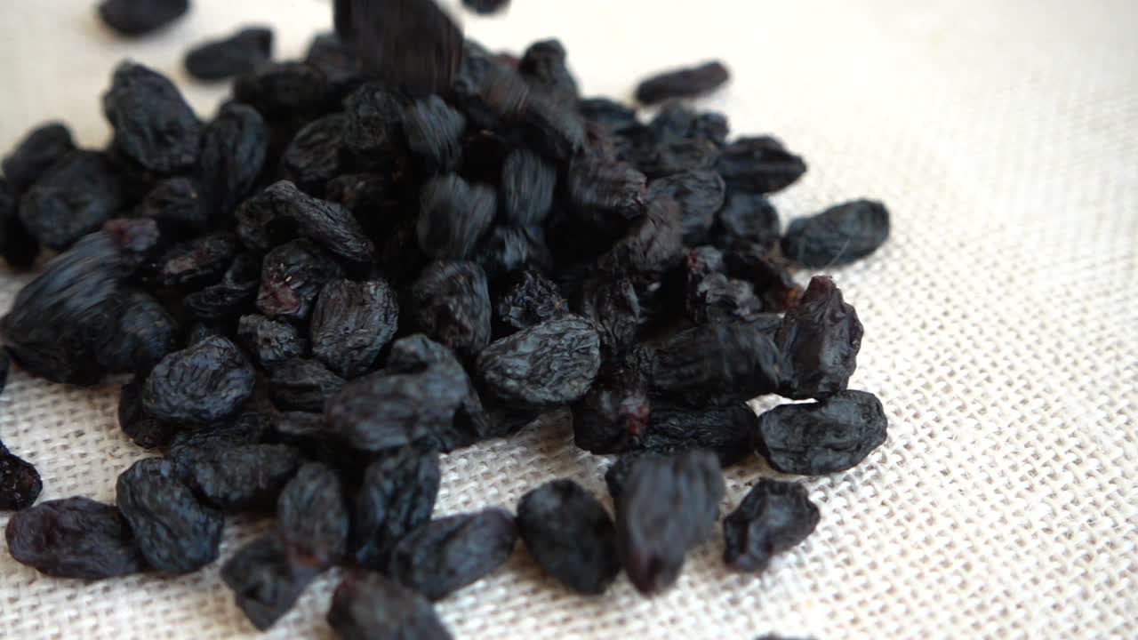 Les raisins secs sont foncés. Filmés en train de tomber sur un sac. Ralenti
