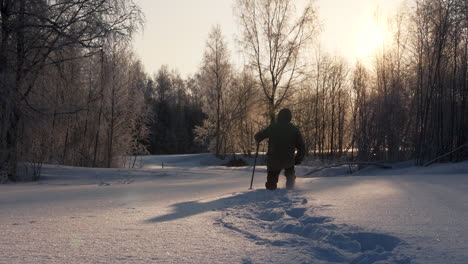 man walks through deep snow in forest during golden hour