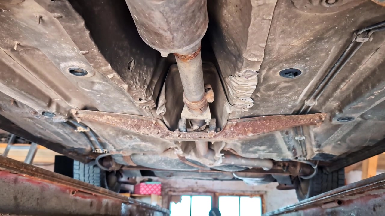 Chassi de carro enferrujado com conversor catalítico e eixo de transmissão vistos por baixo em uma garagem
