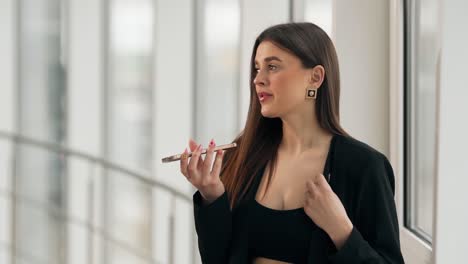 retrato promedio de una joven bonita en un traje de negocios grabando su voz en un teléfono inteligente