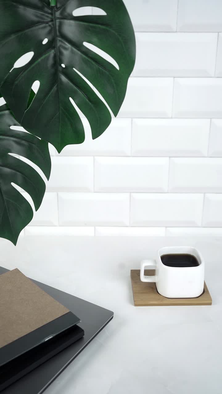 Coffee Cup, Monstera Leaf, and Laptop on a White Desk