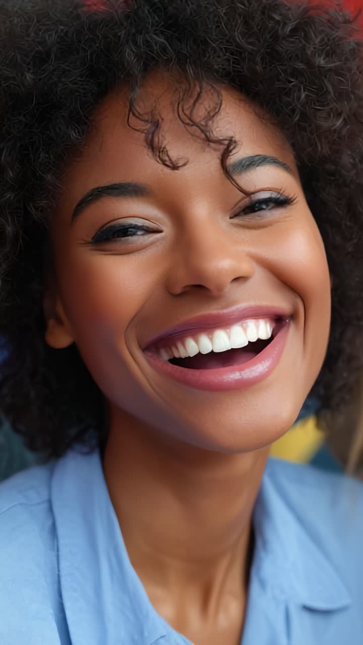 Retrato alegre de uma mulher sorrindo radiantemente com cabelos cacheados em um plano de fundo colorido, capturando a felicidade e o positivismo no dia a dia