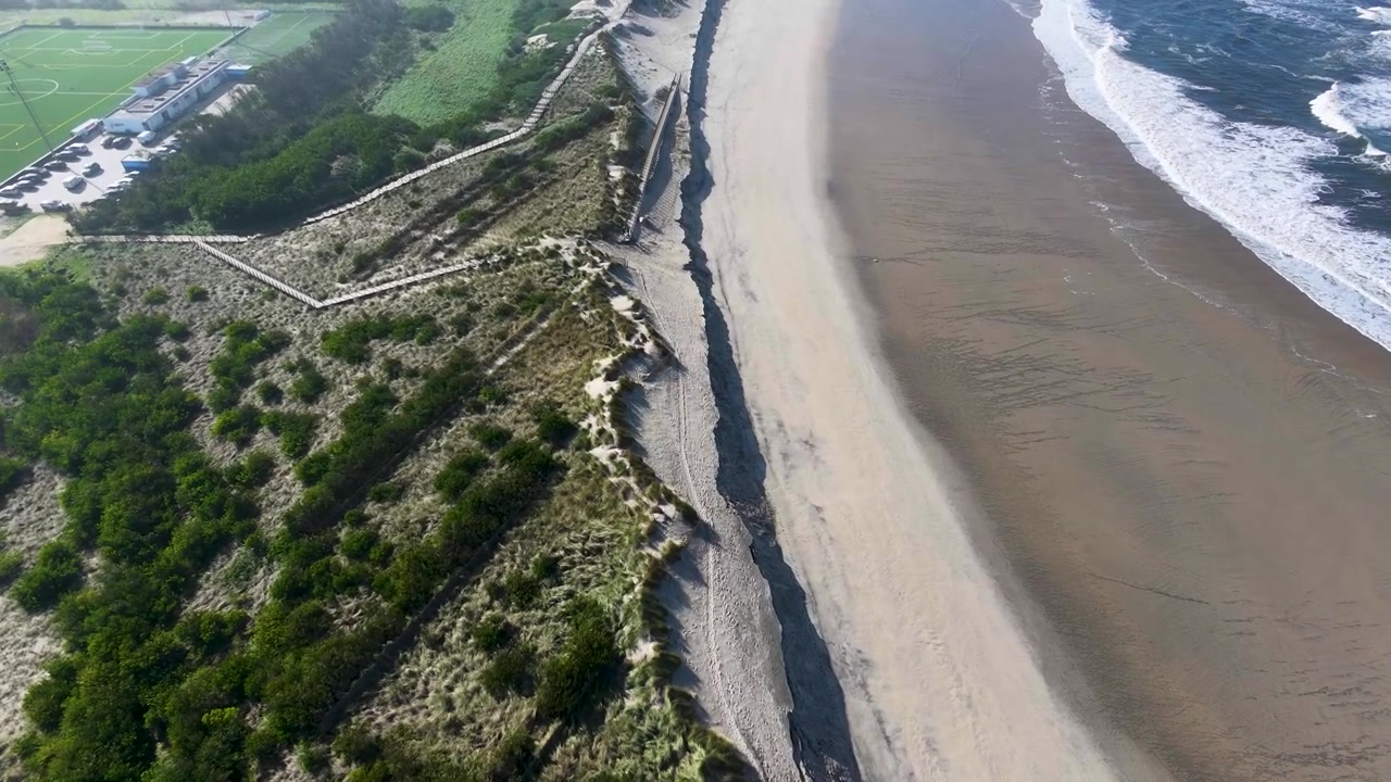 Vista aerea con drone di onde che si infrangono verso una spiaggia sabbiosa e si rompono lungo la riva in una giornata di sole, catturando la bellezza della costa del Portogallo