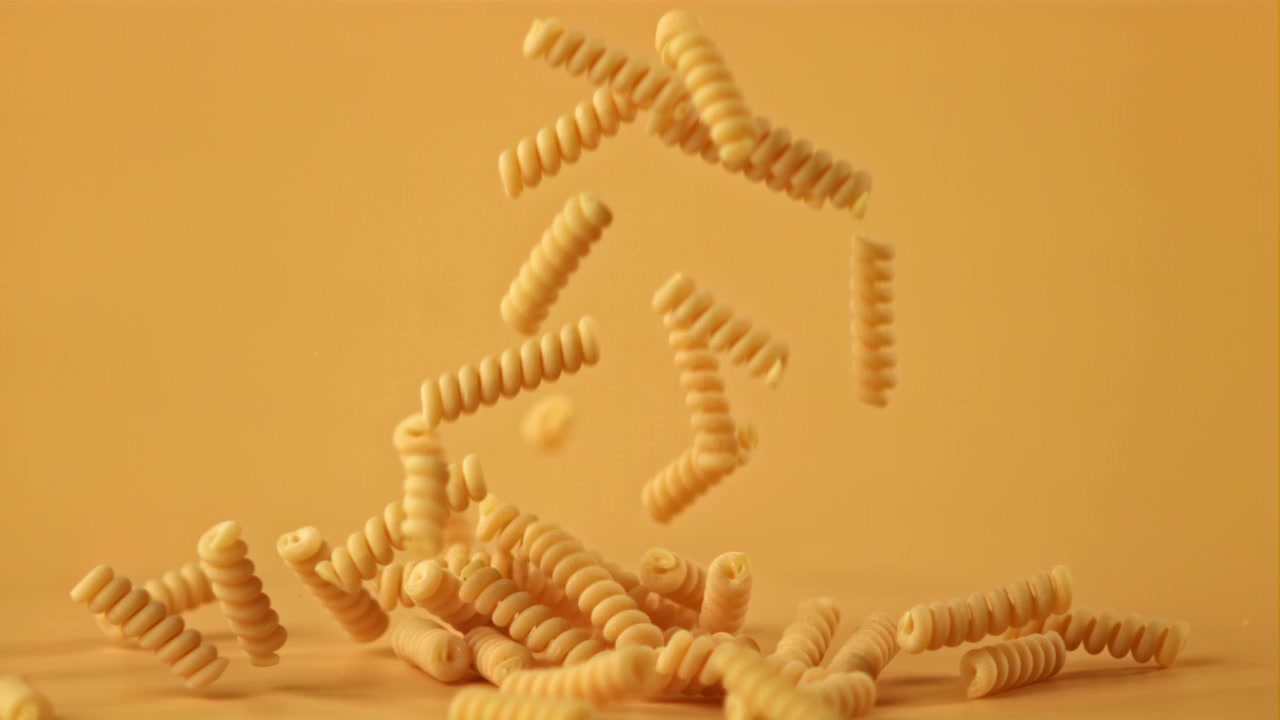Ripresa al rallentatore di pasta secca che cade su uno sfondo giallo