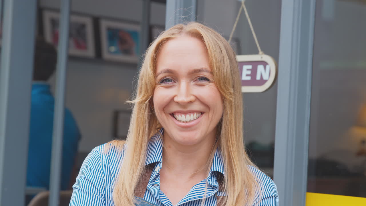 Portret van een vrouwelijke eigenaresse of medewerkster buiten een winkel of café, staand bij een 'Open'-bord in de deuropening