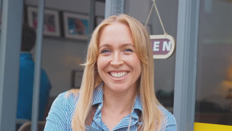 portrait of female owner or staff outside shop or cafe standing by open sign in doorway