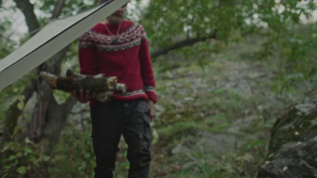 Man Bringing Bundle of Chopped Firewood and Axe to Forest Campsite