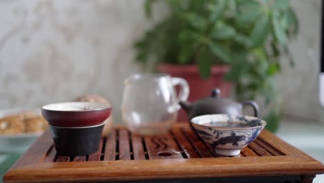 a man's hand pours tea from a transparent teapot into a bowl and pours the rest into a portable table for a tea ceremony