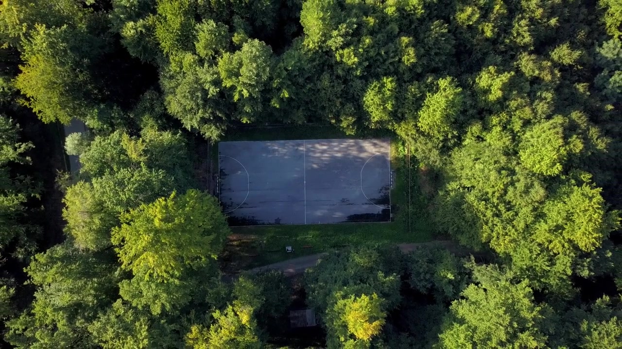 Drone video captures an isolated outdoor sports court amid dense green trees, bathed in natural sunlight, with no people visible anywhere on site.
