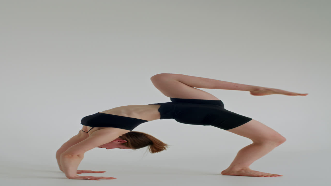 Mädchen übt einbeinige Rad-Pose in einem weißen Yogastudio