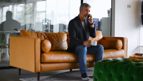 businessman having coffee while talking on mobile phone on sofa 4k