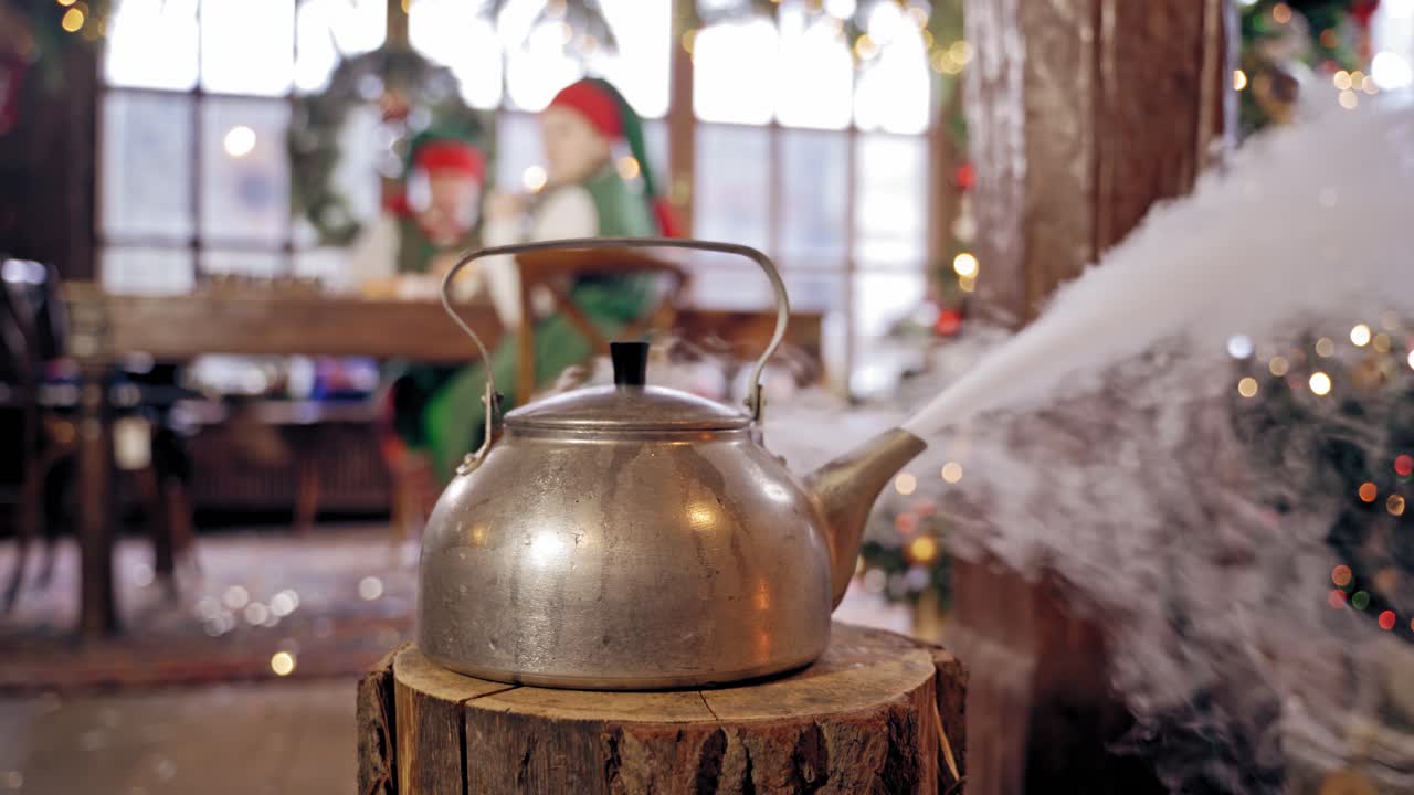 Boiling kettle in the room on blurred Christmas background. Hot kettle with boiled water and white steam on wooden log.