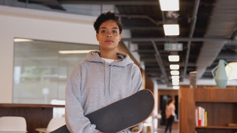 casually dressed young businesswoman with skateboard standing in open plan workplace