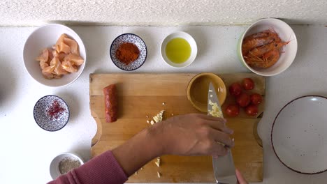 male hands using knife cutting garlic on wooden cooking board, top down view