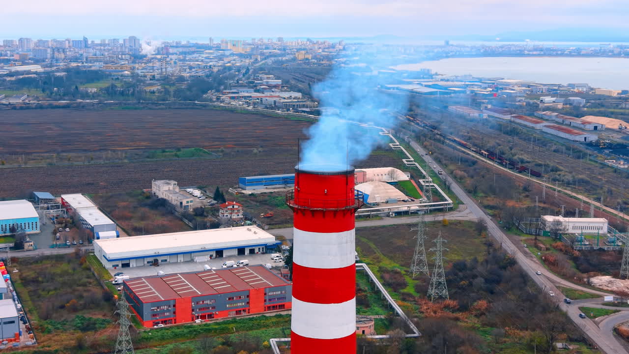 Vista aerea ravvicinata dell'emissione di fumo da una ciminiera. Vista dall'alto di fumo denso che emette da una ciminiera industriale a strisce rosse e bianche vicino al mare