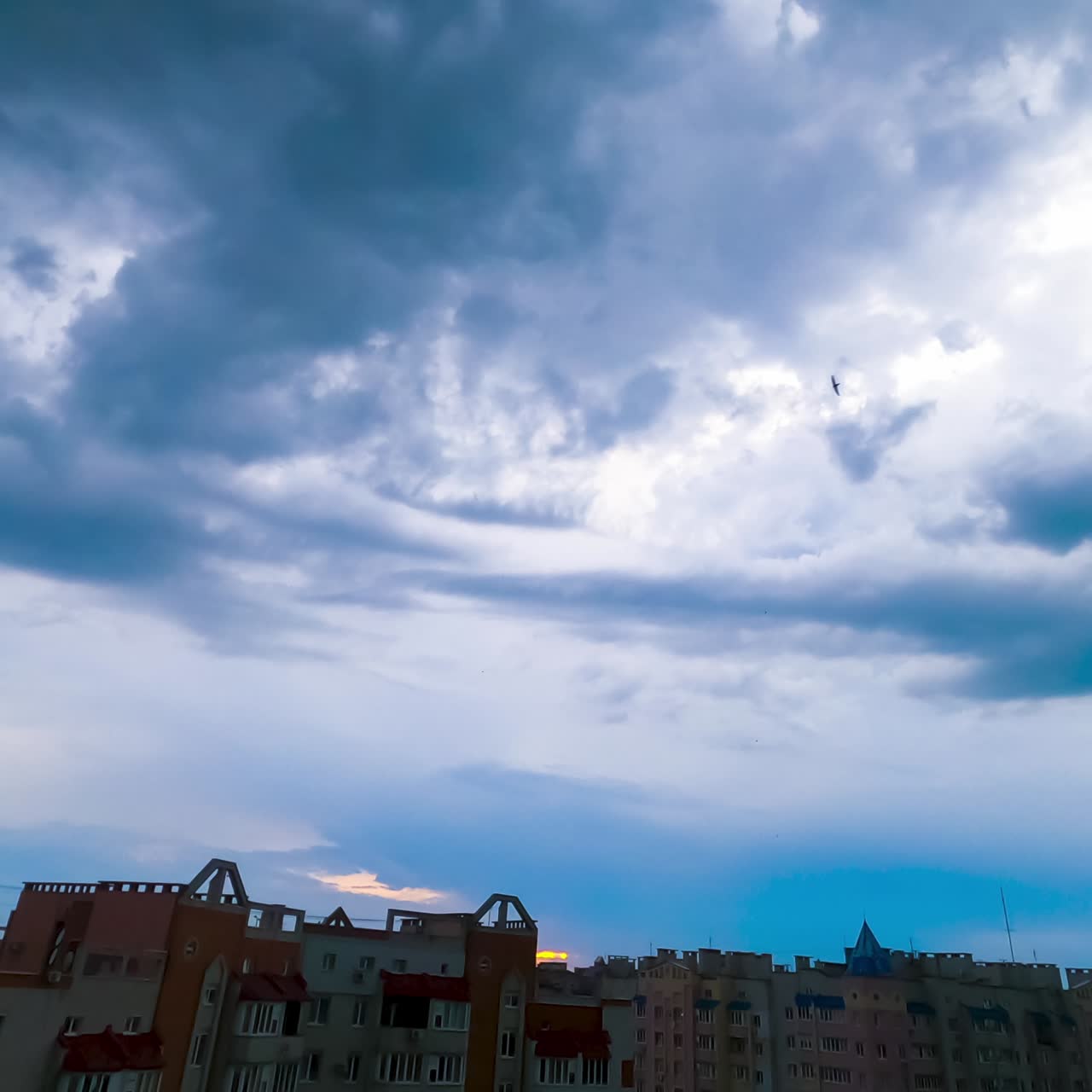 Blue clouds move over the houses in residential area. Timelapse. Yellow splashes appearing in the sky