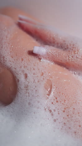 woman applies foam on legs taking in bathtub closeup. graceful lady do pampering spa procedure in bathroom. total relaxation in hot aromatic water