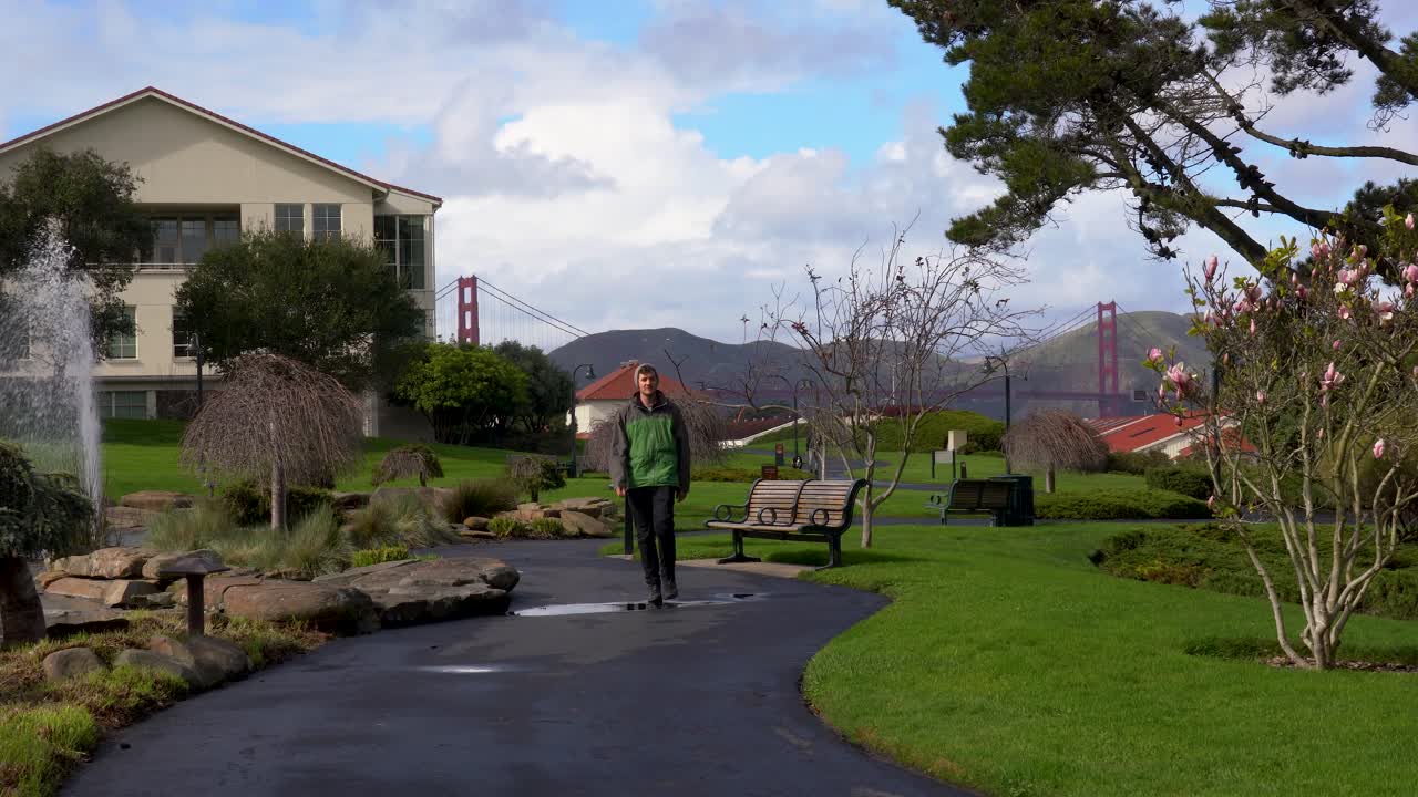 Young man walks curvy path away from Golden Gate Bridge in The Presidio of San Francisco in daytime