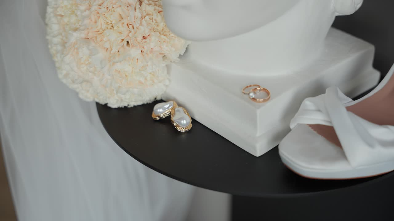 Close-up of elegant bridal accessories including pearl earrings, wedding rings, and a soft floral bouquet on display, capturing a romantic and luxurious wedding preparation scene