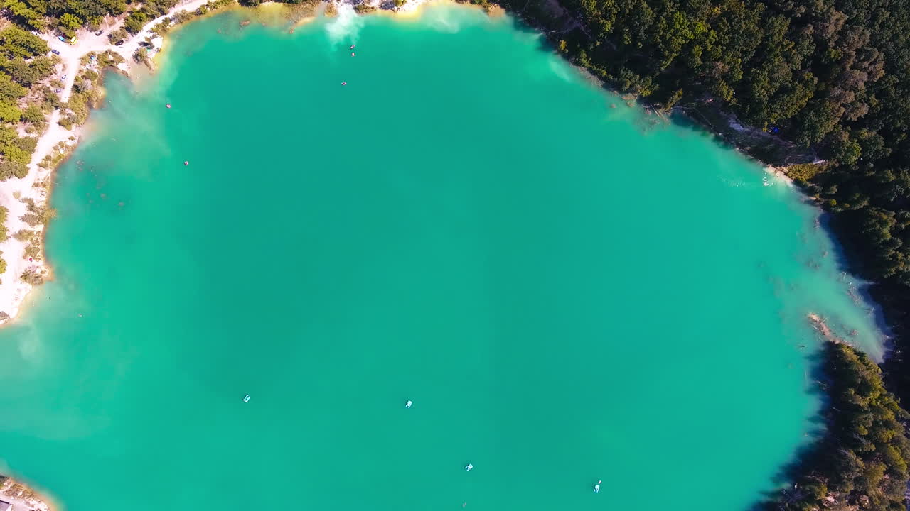 Former kaolin clay mine flooded by water. Few catamarans sailing around the surface. Green thick forests around. Top view.