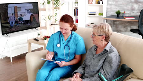 nurse in retirement home taking notes on clipboard while talking with elderly retired woman