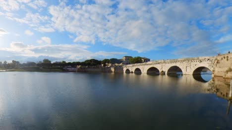 ancient roman bridge over calm river under blue sky