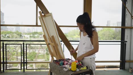 woman painting on an easel in an art studio with city views
