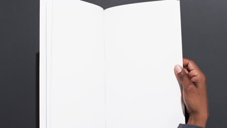 Video-of-hand-of-african-american-man-holding-book-with-blank-pages,-copy-space-on-black-background