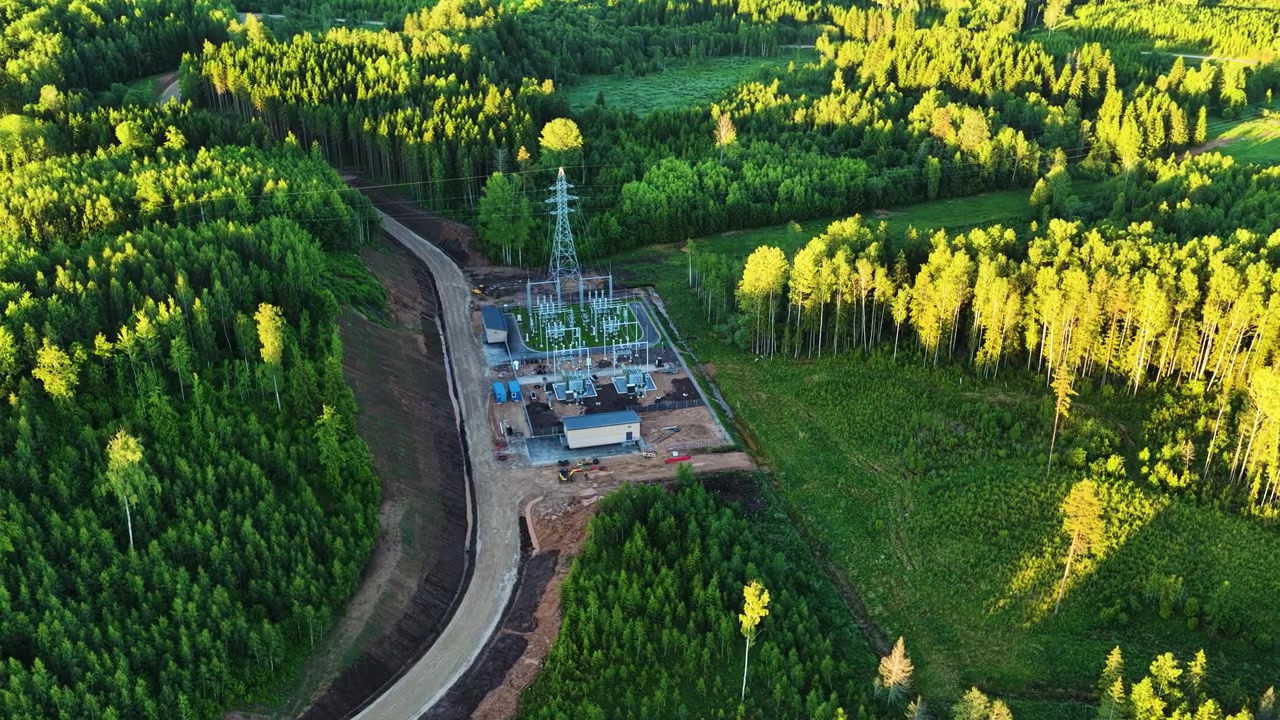 High voltage electrical substation distributing power through a lush green coniferous forest