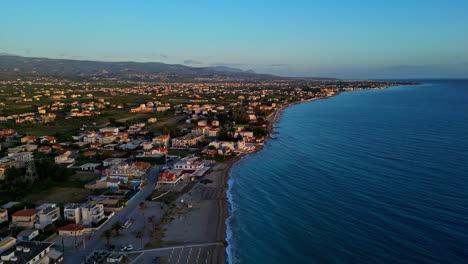 Luftdrohne-Fliegt-über-Den-Strand-Von-Kiato-In-Griechenland,-Küstenstadt-Mit-Panoramablick-Auf-Die-Blaue-Skyline