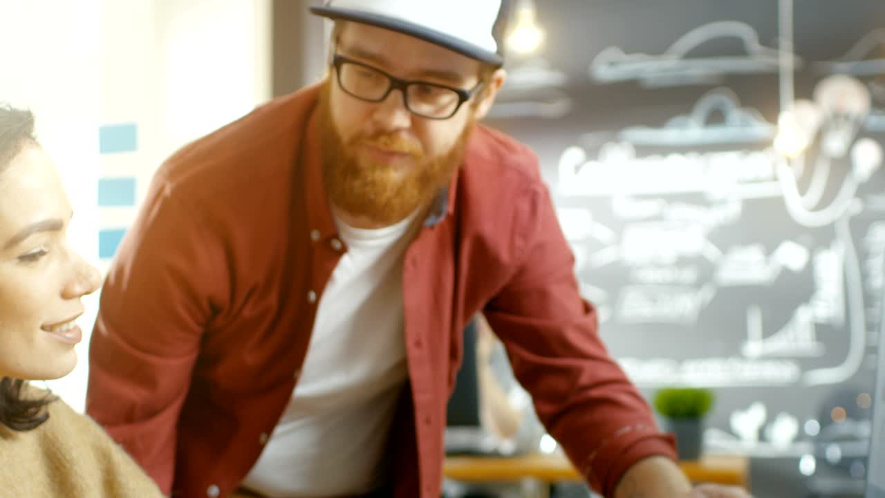 una hermosa desarrolladora usa una computadora personal y habla con un programador, juntos diseñan un nuevo juego móvil o aplicación. trabajan en el elegante estudio creativo indie.