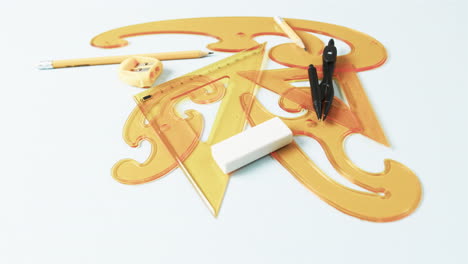 Close up of compass, pencil, sharpener, eraser and rulers on white background, slow motion