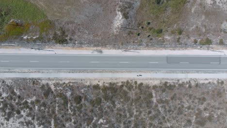 Vista-Vertical-Aérea-De-Una-Carretera-En-Una-Reserva-Natural-Con-Arena-Y-Arbustos-A-Ambos-Lados