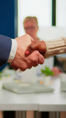 vertical video close up of multiracial business partners standing in front of conference desk shaking hands