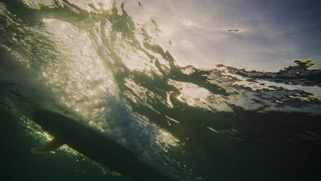 Sparkling-ray-of-light-underwater-from-breaking-wave-with-surfer