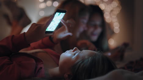 happy-teenage-girls-lying-on-bed-using-smartphone-texting-on-social-media-browsing-online-having-fun-sleep-over-on-weekend-night