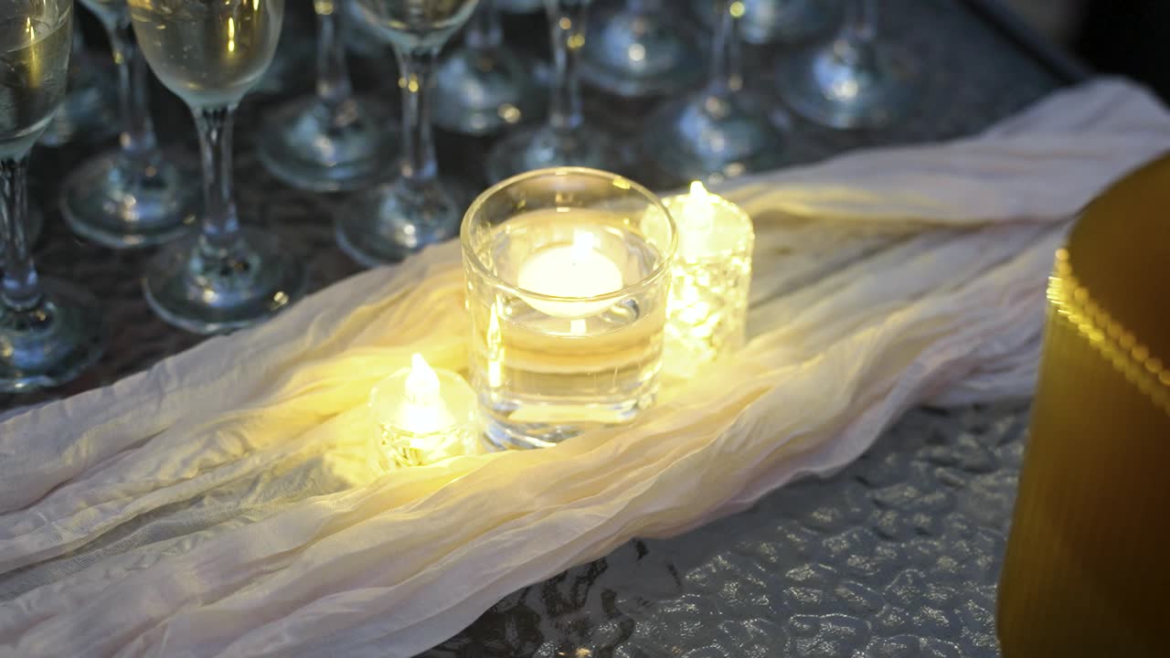 Soft candlelight illuminates a beautifully arranged table setting with glasses and elegant drapes. Ideal for creating a cozy vibe at any event or dinner party