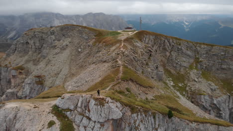 aerial circular shot from a drone of an young male model standing on the edge of a rock in seceda, italy