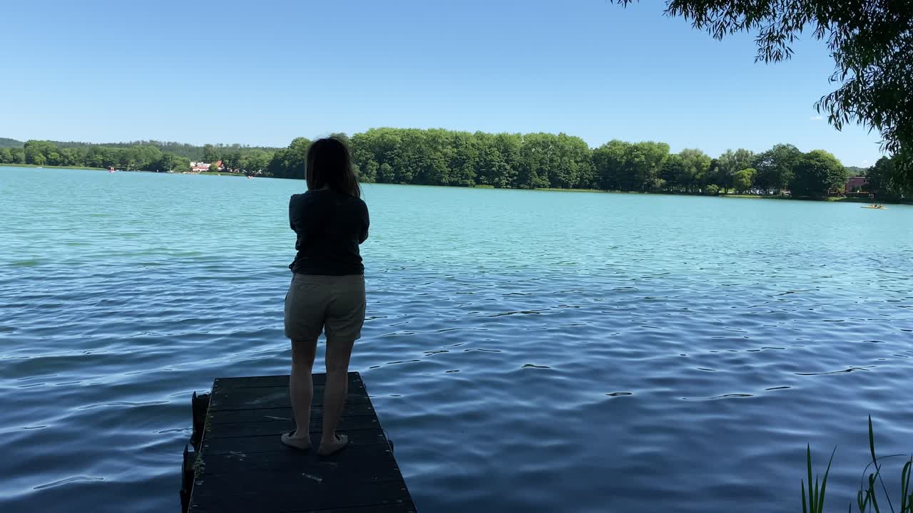 그 소녀는 나무 다리 끝에 서서 그녀의 스마트폰으로 아름다운 전경을 만들고 있다