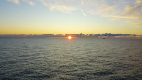 Aerial-shot-as-the-sun-peaks-through-distant-clouds-during-the-early-morning-sunrise-over-water