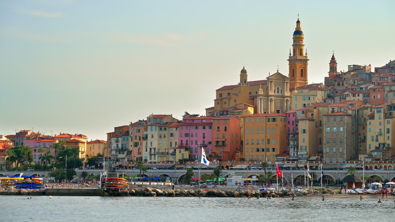People swimming in the sea with a view of the colourful buildings in Menton, France