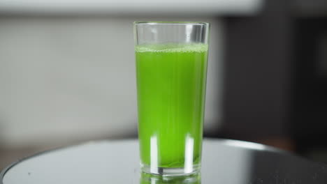 full glass of vibrant green juice with natural light and delicate foam on top