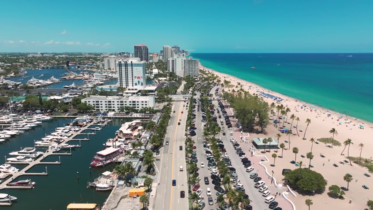 Vistazo aéreo de la energía frente a la playa de Fort Lauderdale: arena dorada, mar esmeralda, condominios modernos y el icónico paseo marítimo de Las Olas vibrando con vida