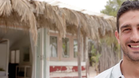 Portrait-of-happy-caucasian-man-looking-at-camera-over-beach-house