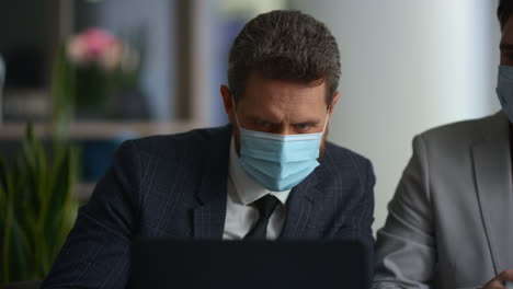 diverse managers team research laptop wear face mask in modern office building.